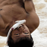 A young Lao fisherman in Khone Falls holds a fish while crossing the rapids of the Li Phi Falls using a single rope.